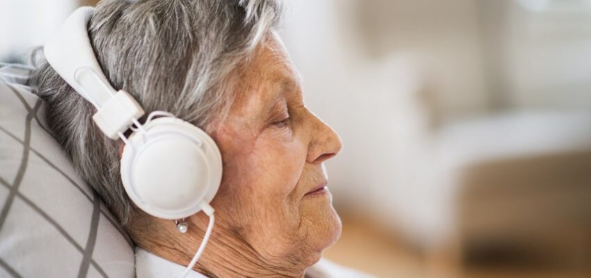 Sick senior woman with headphones lying in bed at home or in hospital.